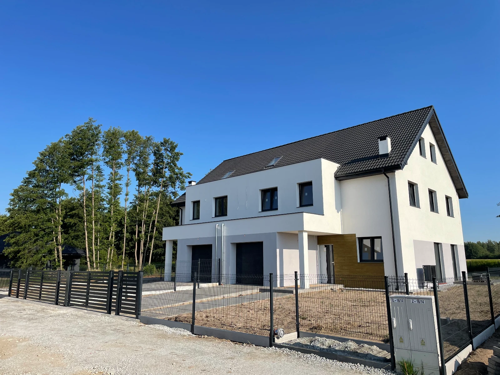 Bliźniaczy budynek mieszkalny w stanie surowym zamkniętym z czarnym dachem i panelowym ogrodzeniem