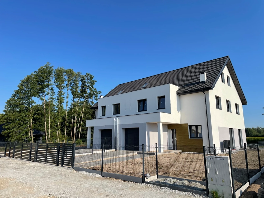 Elewacja domu z białym tynkiem, czarnymi bramami garażowymi i panelowym ogrodzeniem