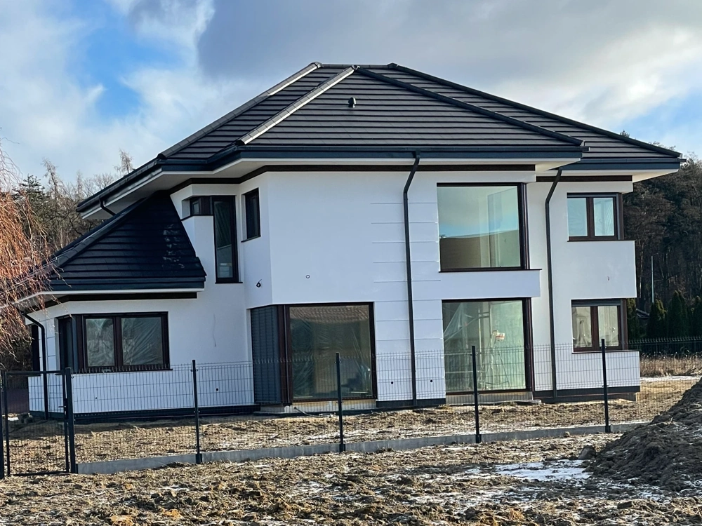 Dwupiętrowy dom jednorodzinny w stanie surowym zamkniętym z białą elewacją i czarnym dachem