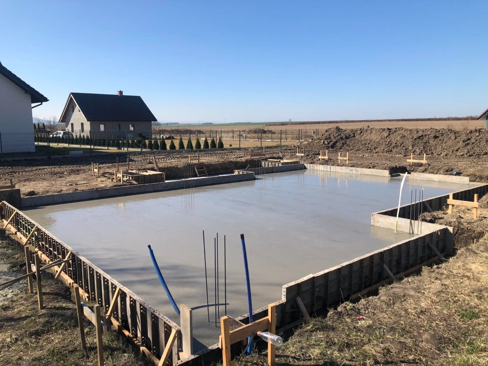 Płyta fundamentowa z widocznym szalunkiem, zbrojeniem i rurami instalacyjnymi na działce budowlanej