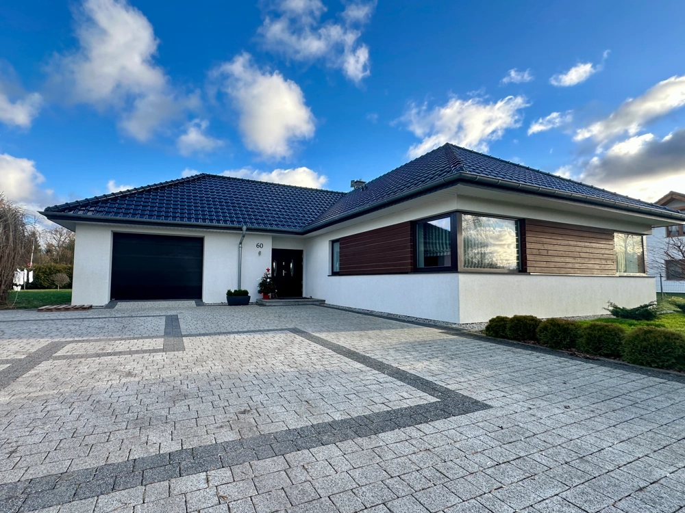 Elewacja domu jednorodzinnego z białym tynkiem i drewnianymi panelami, czarna brama garażowa