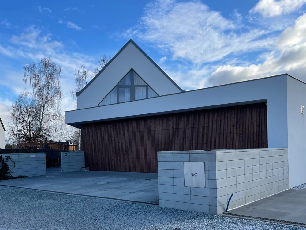 Drewniana brama garażowa na betonowym podjeździe przed nowoczesną białą elewacją domu