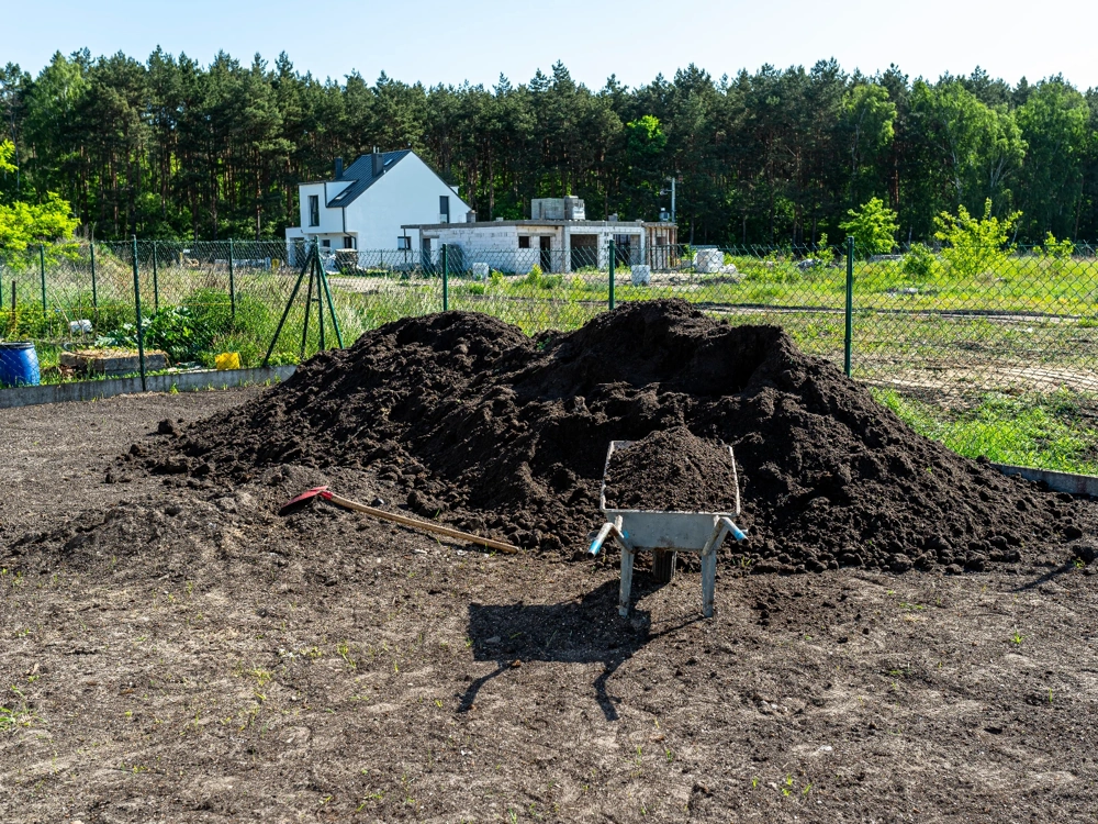 Prace ziemne na działce budowlanej: kopczyk ziemi, taczka i łopata