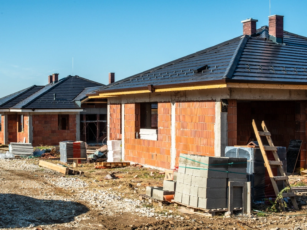 Domy w stanie surowym zamkniętym z murowanymi ścianami i pokryciem dachowym, z materiałami budowlanymi na pierwszym planie