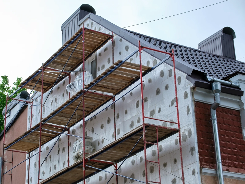 Rusztowanie z płytami styropianowymi na ścianie budynku podczas ocieplania domu