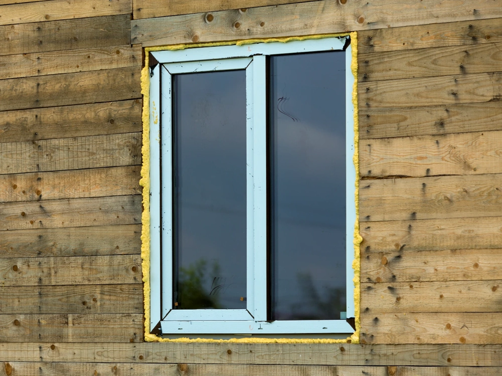 Montaż okien w drewnianej ścianie z widoczną pianką uszczelniającą