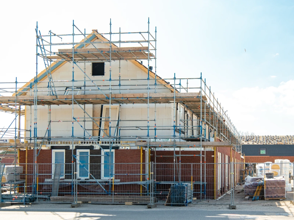 Budowa domu w stanie surowym otwartym z rusztowaniami, murami z cegły i konstrukcją ścian górnej kondygnacji