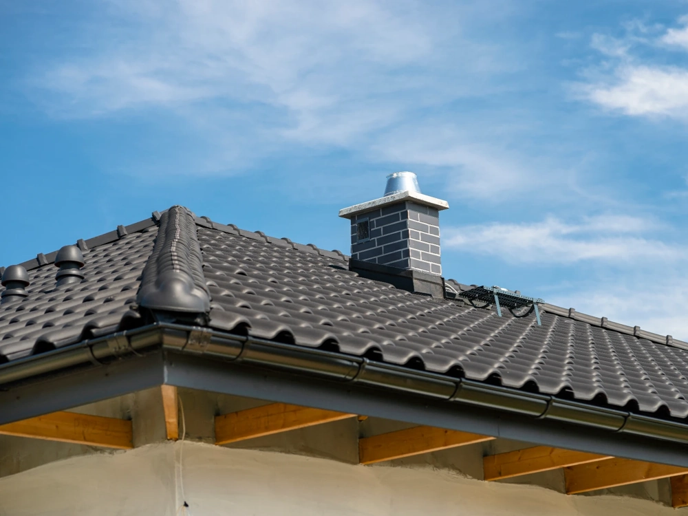 Pokrycie dachowe ciemnoszarymi blachodachówkami i widoczny komin