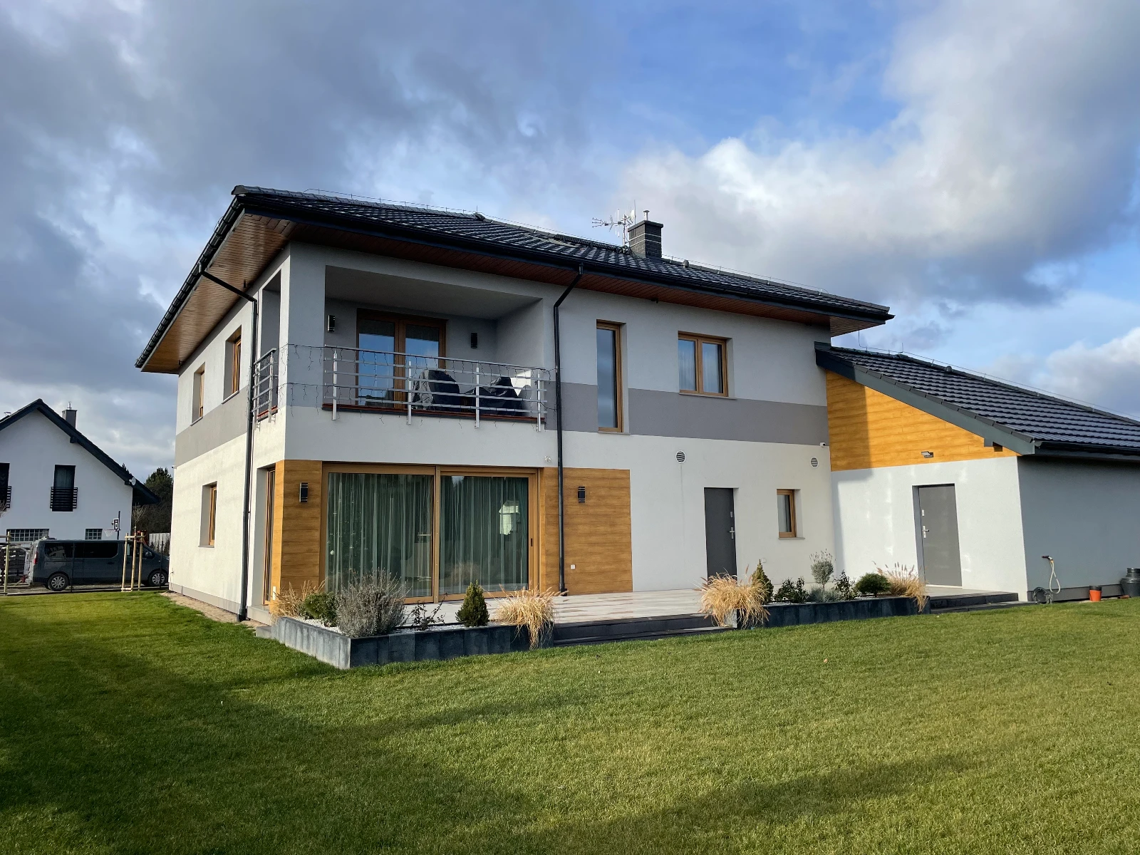 Dwupiętrowy dom jednorodzinny z elewacją domu łączącą biały tynk i drewniane panele, balkonem, dużymi oknami i garażem