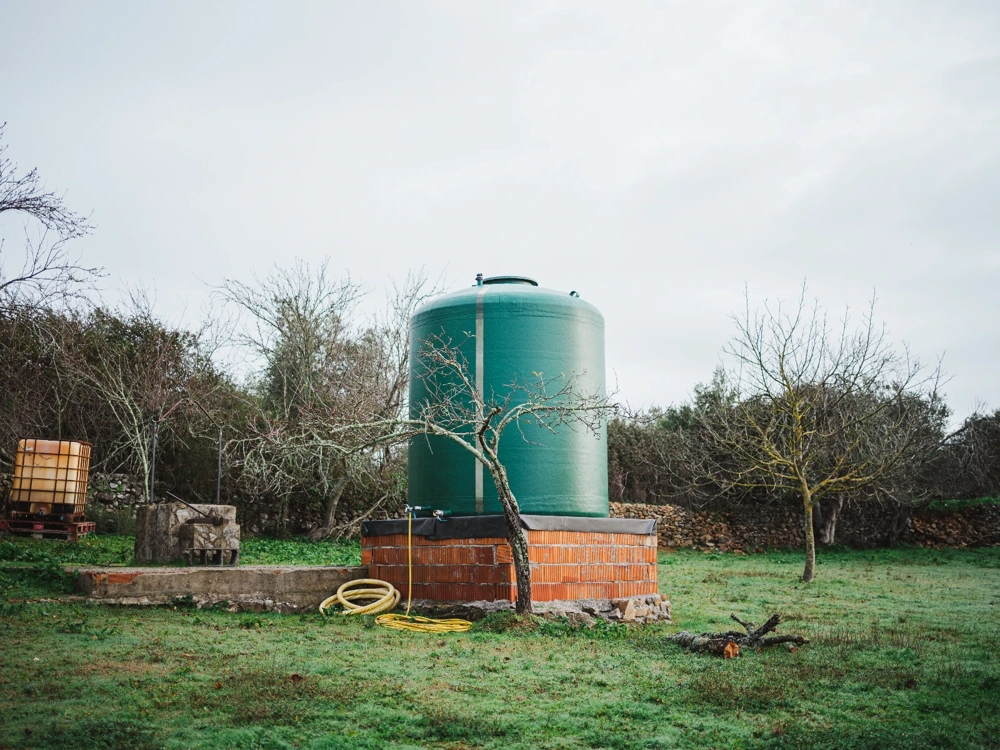 Zielony zbiornik na deszczówkę na murowanej podstawie z wężem w ogrodzie