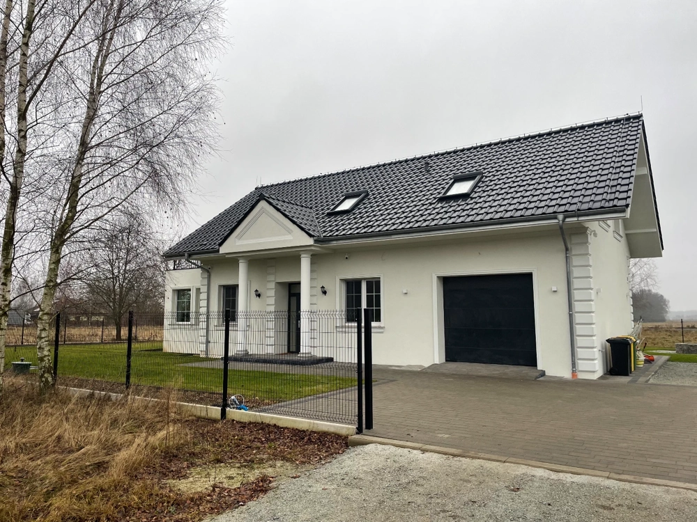 Elewacja domu: biała z kolumnowym wejściem i dachem pokrytym czarnymi dachówkami