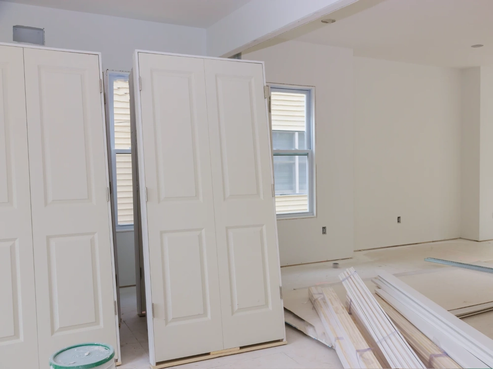 Przygotowane do montażu drzwi wewnętrzne opierające się o ścianę w pomieszczeniu w stanie deweloperskim Montaż drzwi