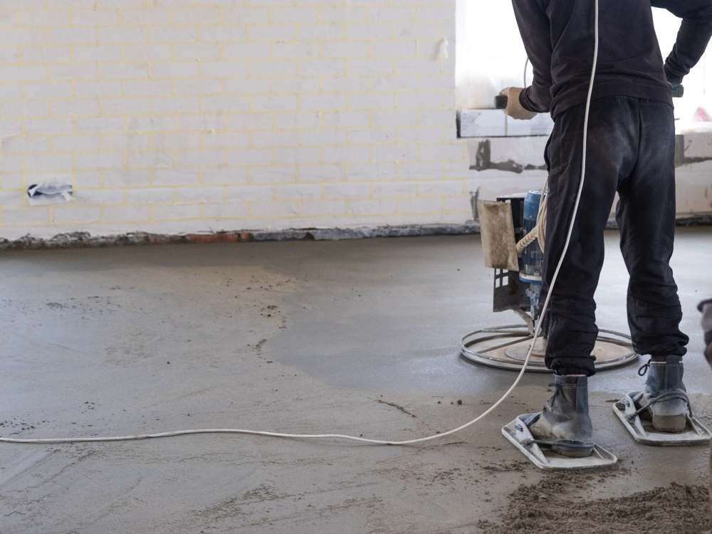 Posadzki betonowe: pracownik z maszyną do zacierania wyrównuje świeżą wylewkę