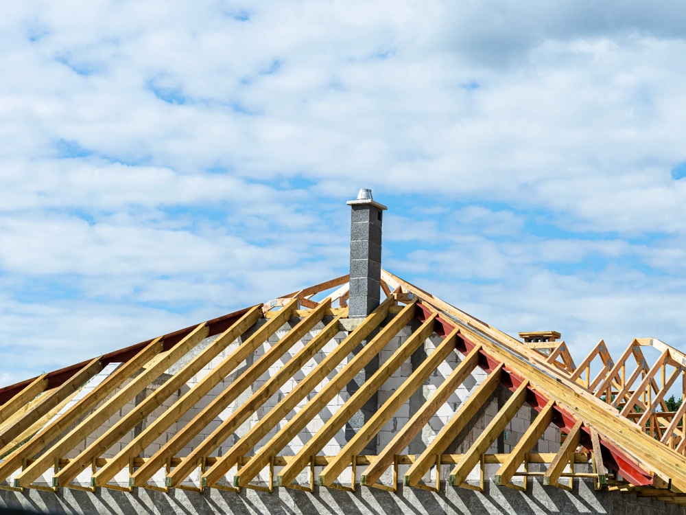 Montaż więźby dachowej z drewnianymi krokwiami i kominowym przewodem na budowie dachu