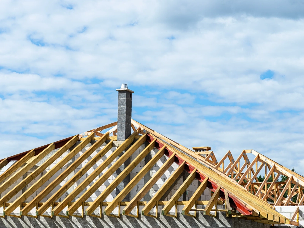 Więźba dachowa domu jednorodzinnego z drewnianymi krokwiami i murowanym kominem