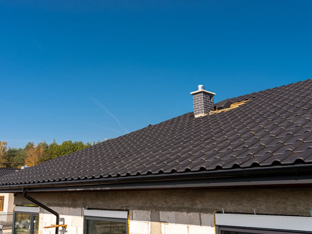 Pokrycie dachowe z ciemnych dachówek na budynku z widocznym kominem i nieukończoną elewacją
