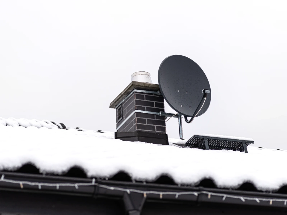 Komin na zaśnieżonym pokryciu dachowym z zamontowaną anteną satelitarną