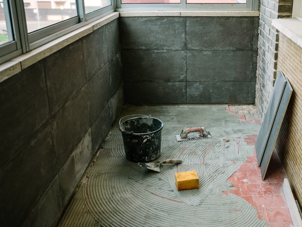 Układanie posadzki z płytek, wiaderko z zaprawą, kielnia i gąbka na balkonie