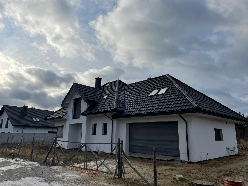Biały nowoczesny dom z czarnym pokryciem dachowym i garażem w otoczeniu budowy