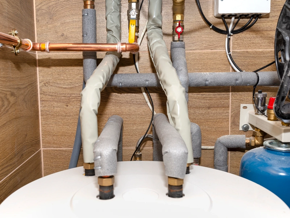 Instalacje hydrauliczne: izolowane rury i zawory przy zbiorniku ciepłej wody